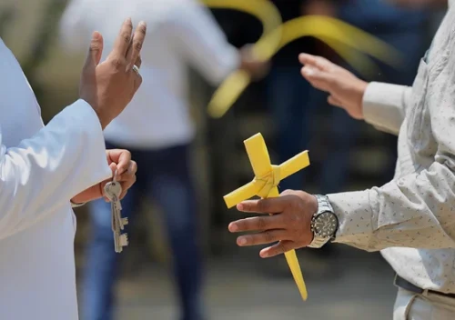 Zdroj: Manjunath Kiran / Getty Oddaný křesťan drží kříž, vyrobený z palmového listu, během hovoru s pastorem.